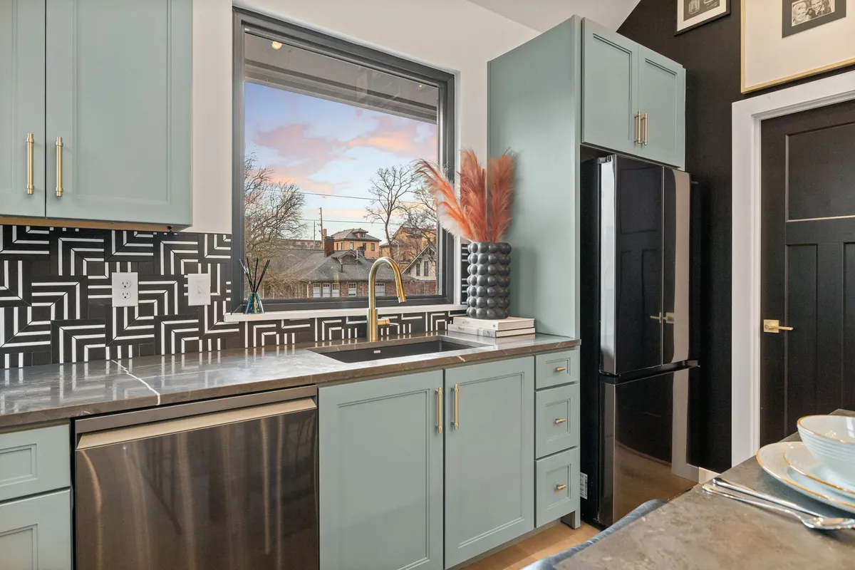 A chic, contemporary kitchen with sleek stainless steel appliances, geometric backsplash, and a window with a scenic view. The inviting island is perfect for meal prep or casual socializing, and a decorative vase adds a touch of local artistry.