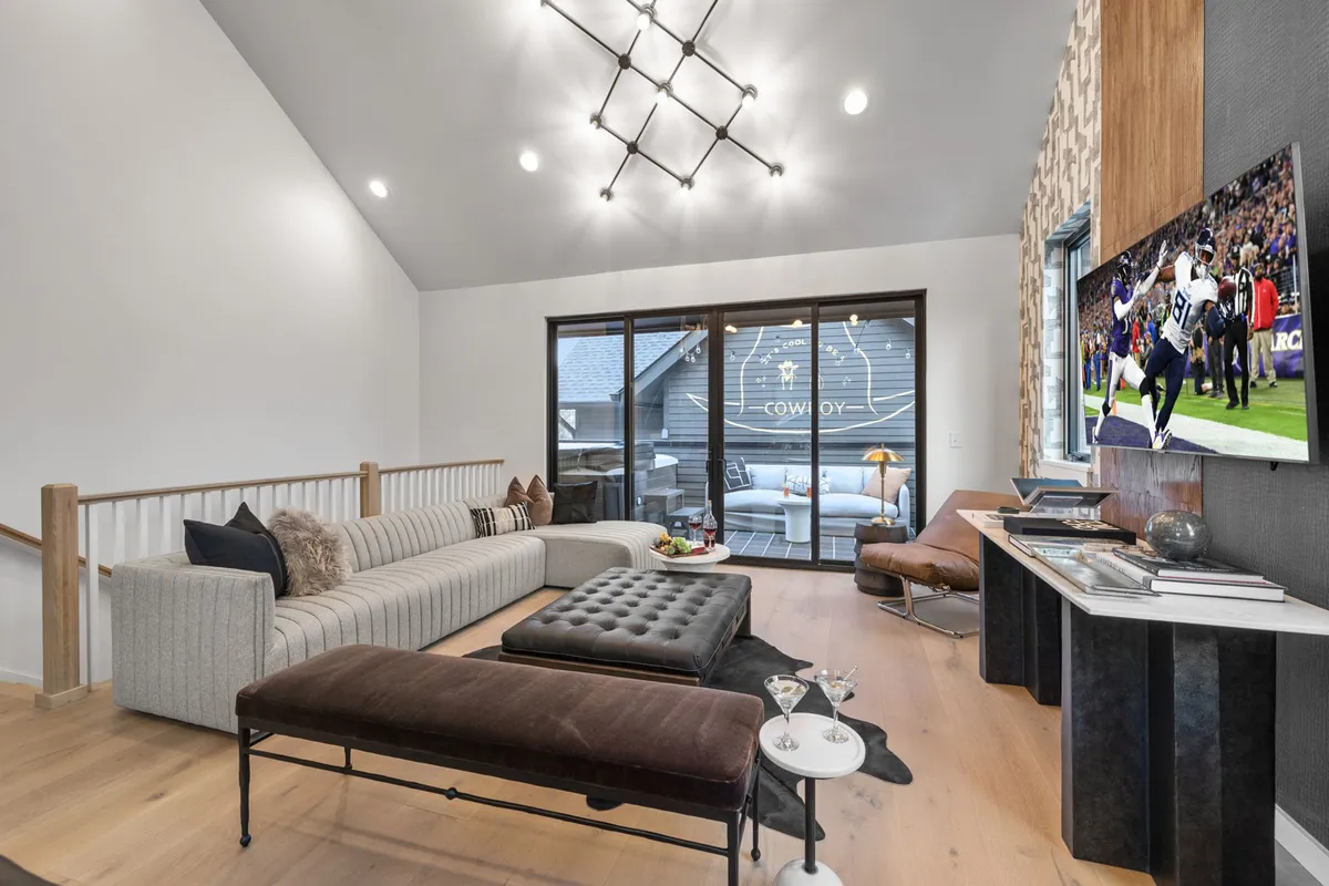 A stylish living room with a sectional sofa, coffee table, TV, and sliding glass doors opening to a private balcony. The space is designed for comfort and entertainment, with a seamless flow to the outdoors.