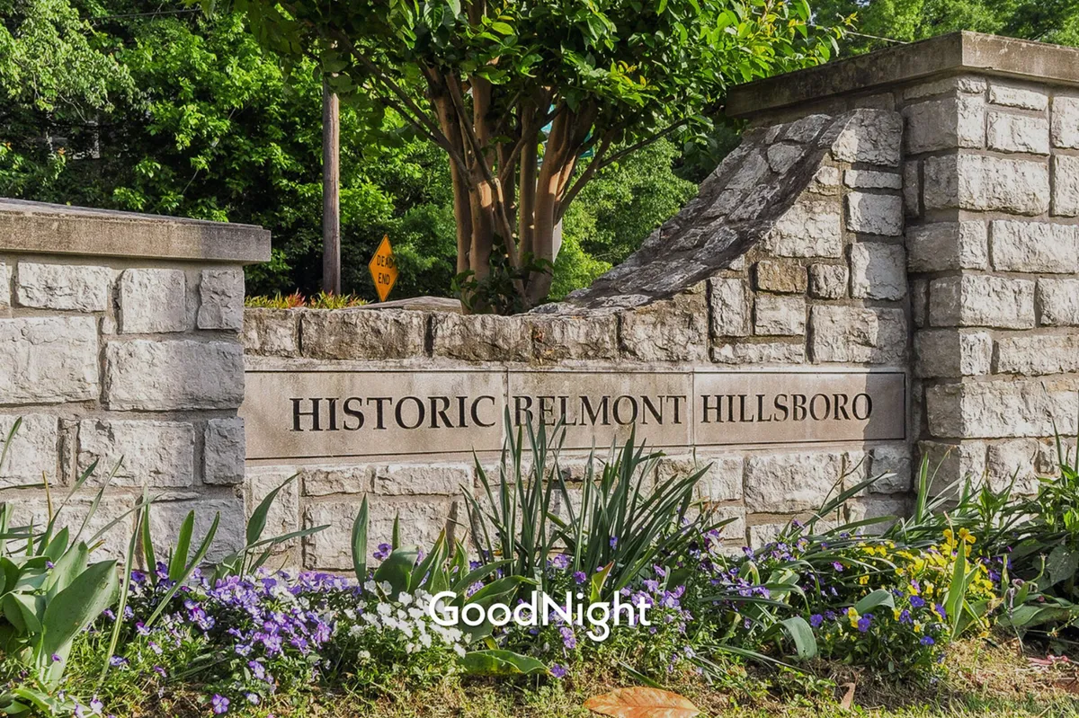 A stone entrance sign surrounded by lush greenery and vibrant, colorful flowers. The inviting pathway hints at nearby parks and accessible green spaces, ideal for dog walks and outdoor exploration.