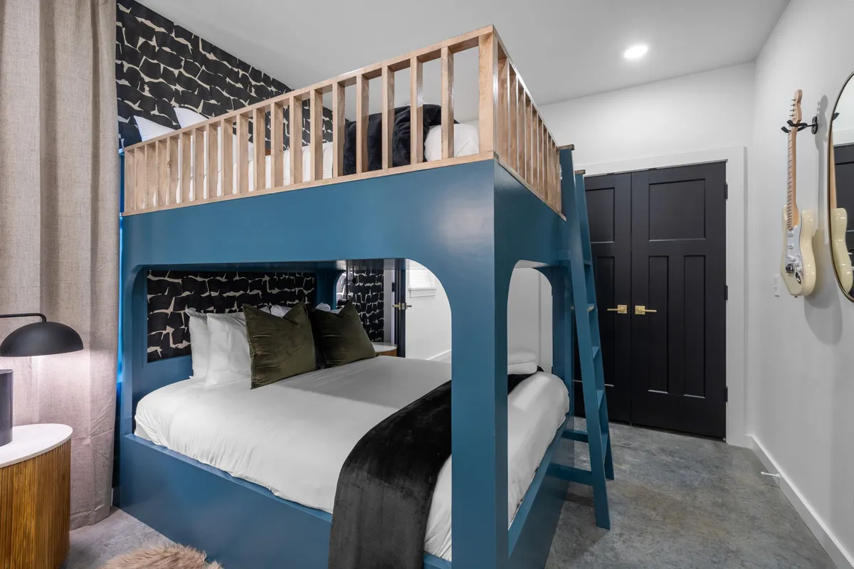 A playful bunk room with a queen-over-queen bunk bed set against a decorative wall. The space is well-lit with a cheerful lamp, providing an inviting and fun atmosphere ideal for families or groups of friends.